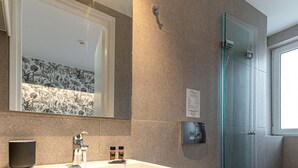 A modern bathroom with a white sink, a glass shower enclosure, and a toilet. - Kriel Suites by LIV Homes 203 (Athens)