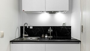 A compact kitchen with white cabinets, a black countertop, and a stainless steel sink. - Kriel Suites by LIV Homes 203 (Athens)