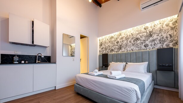 A modern hotel room with a large bed, a built-in wardrobe, a kitchen area, and a bathroom. - Kriel Suites by LIV Homes 302 (Athens)
