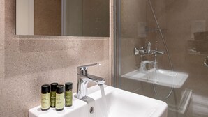 A modern bathroom with a white sink, a glass shower enclosure, and a mirror above the sink. - Kriel Suites by LIV Homes 302 (Athens)