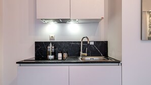 A compact kitchen with white cabinets, a black marble countertop, and a stainless steel sink. - Kriel Suites by LIV Homes 302 (Athens)