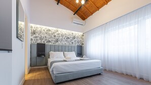 A modern bedroom with a wooden ceiling, a large bed, a wall-mounted air conditioner, and a window with sheer curtains. - Kriel Suites by LIV Homes 302 (Athens)