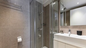 A modern bathroom with a glass-enclosed shower, a white sink, and a large mirror. - Kriel Suites by LIV Homes 202 (Athens)