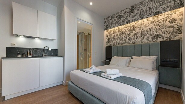 A modern hotel room with a large bed, a built-in desk, and a shower area. - Kriel Suites by LIV Homes 202 (Athens)