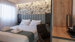 Quarto de hotel com cama, escrivaninha, cadeira e televisão.