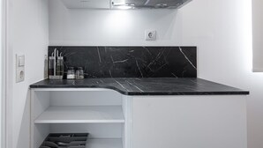 A compact kitchen with white cabinets, a black marble countertop, and a stainless steel range hood. - Kriel Suites by LIV Homes 304 (Athens)