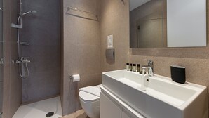 A modern bathroom with a walk-in shower, a toilet, and a large sink with a mirror above. - Kriel Suites by LIV Homes 304 (Athens)