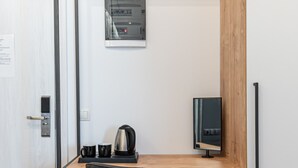 A compact workspace with a wooden desk, a black chair, a coffee maker, and a monitor. - Kriel Suites by LIV Homes 304 (Athens)