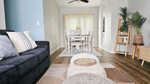A modern living room with a dark grey sofa, a white dining table with chairs, and a ceiling fan. - Pinellas Perch: 3/2 central home, 10 mins to DTSP (Pinellas Park)