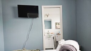 A hotel room with a bed, a TV mounted on the wall, a bathroom visible through an open door, and a tray with towels. - Pinellas Perch: 3/2 central home, 10 mins to DTSP (Pinellas Park)