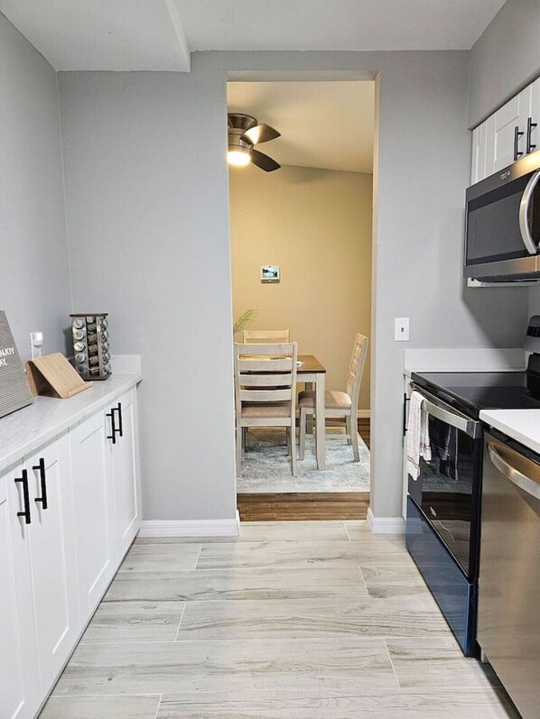 A kitchen with white cabinets, a black countertop, and a wooden dining table with chairs. - Pinellas Perch: 3/2 central home, 10 mins to DTSP (Pinellas Park)