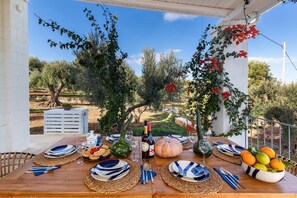 An outdoor dining area with a wooden table set for a meal, surrounded by olive trees and a view of the countryside. - 3686 Villa de Bellis by Perle di Puglia (Fasano)
