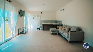 A spacious living area with a sofa, a coffee table, and a TV mounted on the wall. - Maison Avec Piscine, Jacuzzi, Sauna et Billard (Le Thor)
