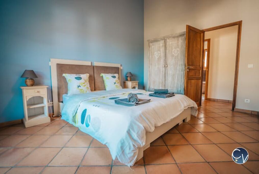 A bedroom with a bed, two bedside tables, a wardrobe, and a door leading to another room.
