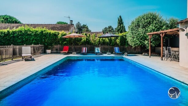 A rectangular swimming pool with a wooden deck surrounding it, a pergola, and a fenced area with chairs and umbrellas. - Maison Avec Piscine, Jacuzzi, Sauna et Billard (Le Thor)