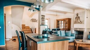 A modern kitchen with a central island, pendant lighting, and a dining area with a sofa and table. - Maison Avec Piscine, Jacuzzi, Sauna et Billard (Le Thor)