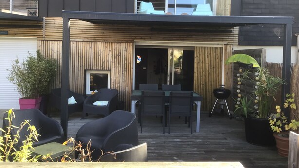 En modern uteplats med plats för matbord, sittmöbler och krukväxter.