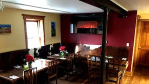 A dining area with wooden tables and chairs, a red wall, and a window with a view. - 1882 Bar and Grill at River Street Inn (Truckee)