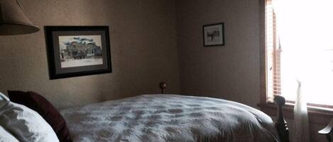 A bedroom with a bed, a framed picture on the wall, and a window with blinds.