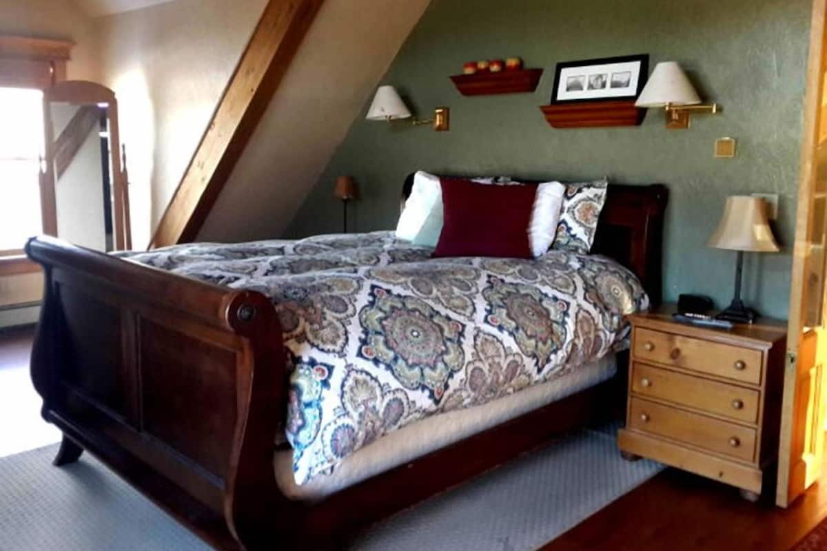 A bedroom with a large bed, wooden headboard, a nightstand with a lamp, and a dresser.