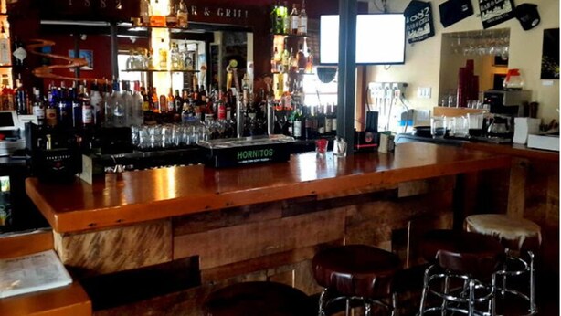 A bar area with a wooden counter, stools, and a variety of bottles and glasses. - 1882 Bar and Grill at River Street Inn (Truckee)