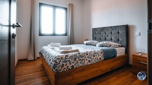 A bedroom with a wooden bed, a grey upholstered headboard, and a window with curtains. - Modern villa with Jacuzzi near Avignon (Le Thor)
