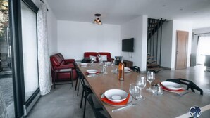 A dining area with a long table set for six, red upholstered chairs, a television mounted on the wall, and a staircase leading to another level. - Modern villa with Jacuzzi near Avignon (Le Thor)