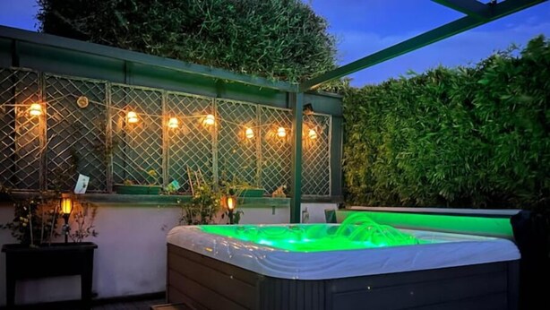 A hot tub with a green light, surrounded by wooden decking and a pergola with string lights. - Modern villa with Jacuzzi near Avignon (Le Thor)