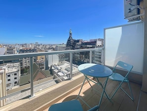 Un balcon avec une table et des chaises, donnant sur un paysage urbain dominé par une tour imposante.