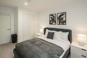A bedroom with a bed, bedside tables, a wardrobe, and abstract wall art. - Stunning 3-bed Apartment in London (London)