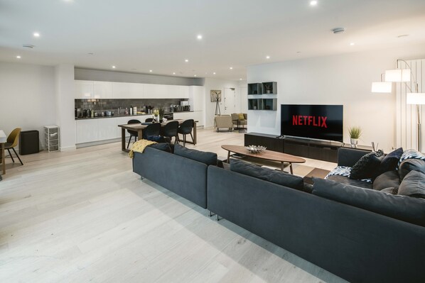 A modern living room with a large sofa, a coffee table, and a TV displaying 'NETFLIX'. - Stunning 3-bed Apartment in London (London)