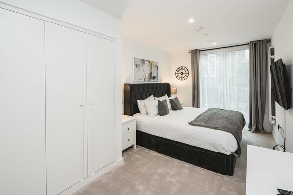 A bedroom with a bed, bedside table, wardrobe, and a large window with curtains. - Stunning 3-bed Apartment in London (London)