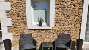 A stone wall with a window, two wicker chairs, a small table, and a potted plant. - Petit Paradis Avec Piscine Partagée (Gizay)