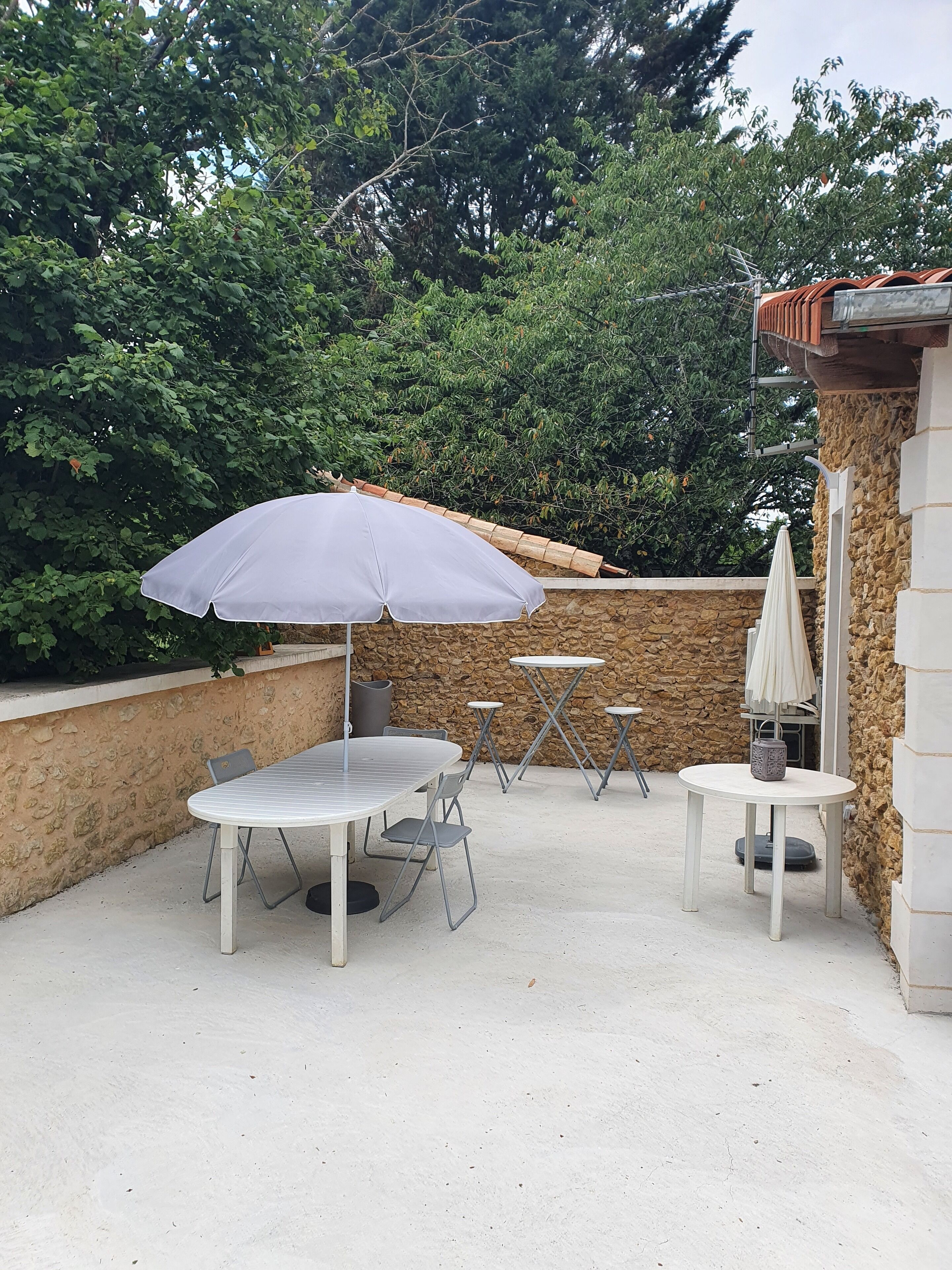 An outdoor patio area with a round table, two chairs, a folding table, and an umbrella.