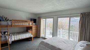 Une chambre avec un lit superposé, un lit simple, un bureau et une fenêtre donnant sur un balcon.