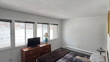 A bedroom with a bed, a dresser, a television, and a window with a view of buildings.