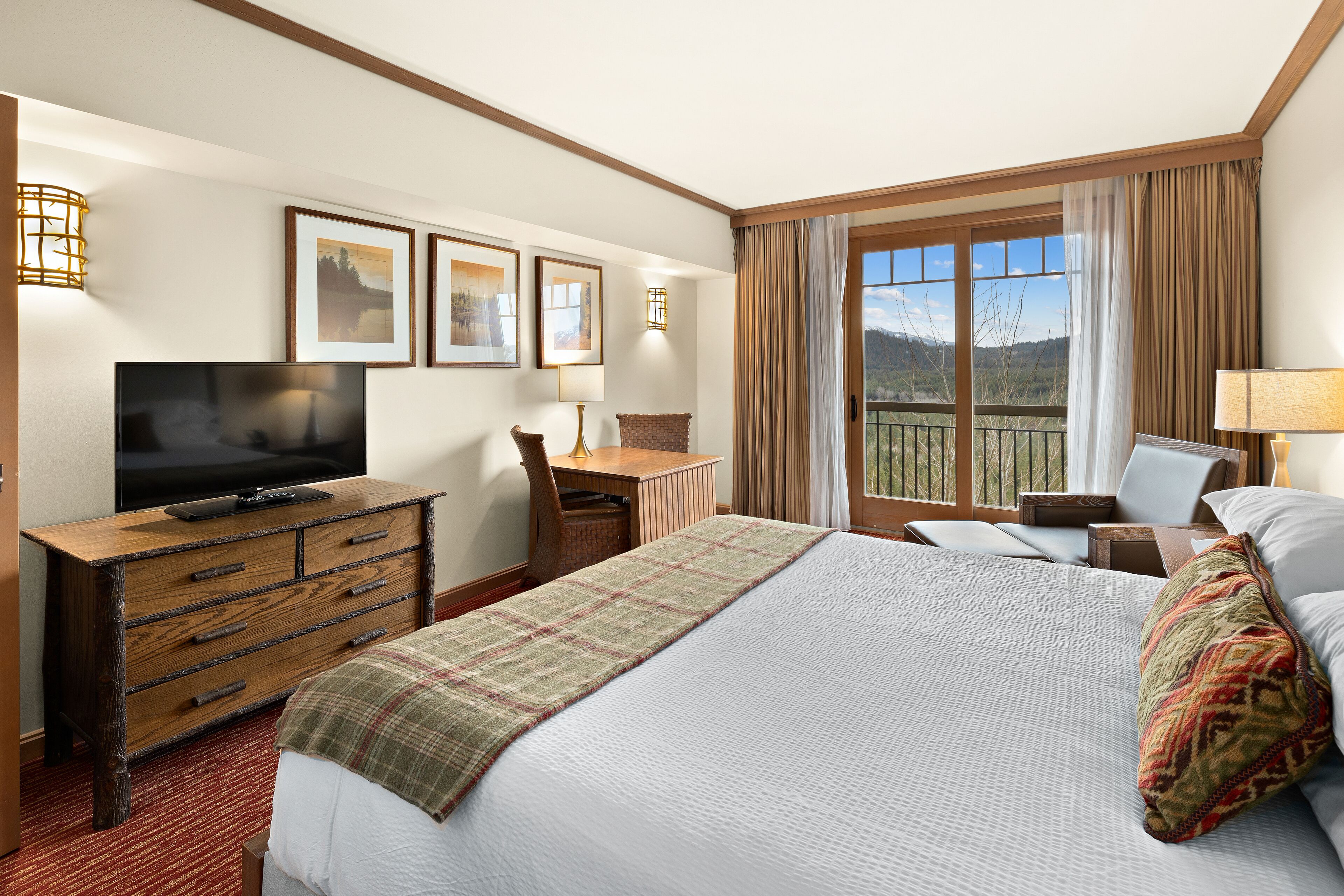 Une chambre d’hôtel avec un grand lit, une commode en bois avec un téléviseur, un bureau avec une chaise et un balcon avec des rideaux.