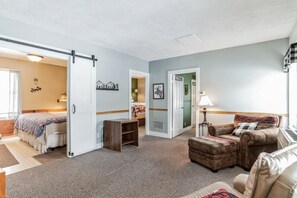 Ein geräumiger Wohnbereich mit einer Couch, einem Hocker und einem Bett mit Kopfteil.