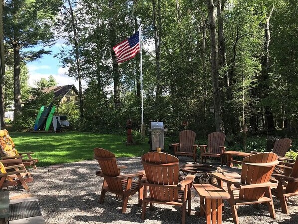 Ein Sitzbereich im Freien mit Adirondack-Stühlen, einem Grill und einer Flagge.