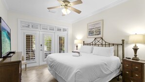 Habitación de hotel con cama, l ámparas de noche, mesita de madera, televisor y ventana con contraventanas.