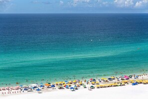A beach with white sand, clear turquoise water, and numerous colorful umbrellas.