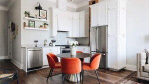 A modern kitchen with white cabinetry, a stainless steel refrigerator, and a dining table with orange chairs. - Ulysses Suites, Suite 201, 2 bedroom/2 bath, full kitchen and living room (Galena)