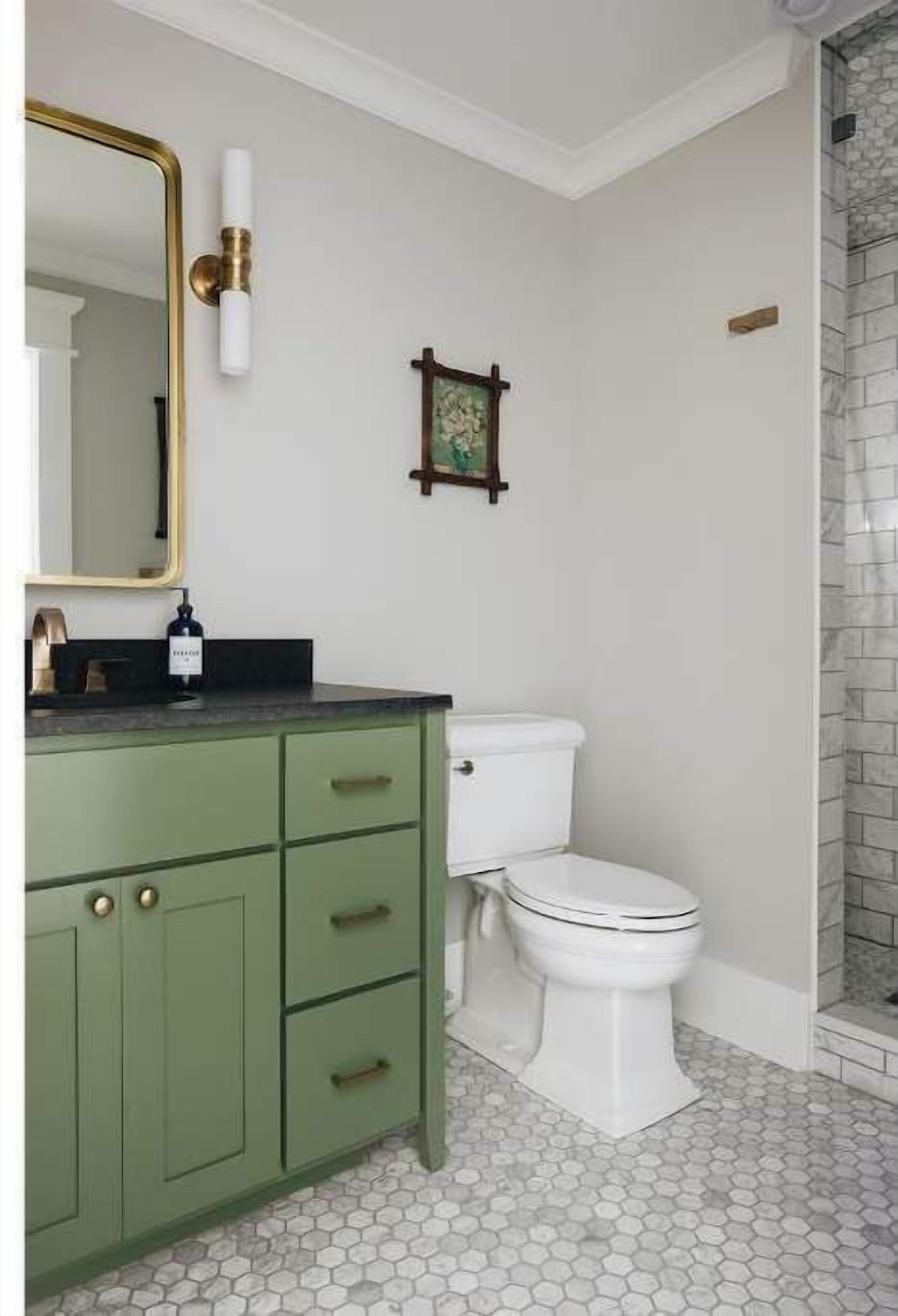 A bathroom with a green vanity, a white toilet, a hexagonal tiled floor, and a shower area with a stone wall.