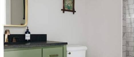 A bathroom with a green vanity, a white toilet, a hexagonal tiled floor, and a shower area with a stone wall.