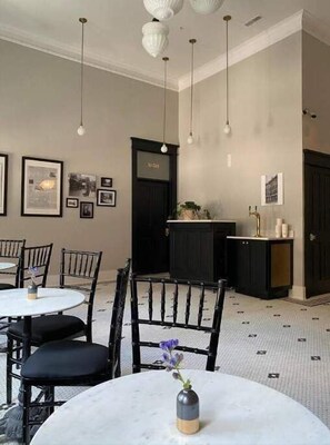 Un comedor con mesas y sillas redondas, un aparador negro y lámparas colgantes.