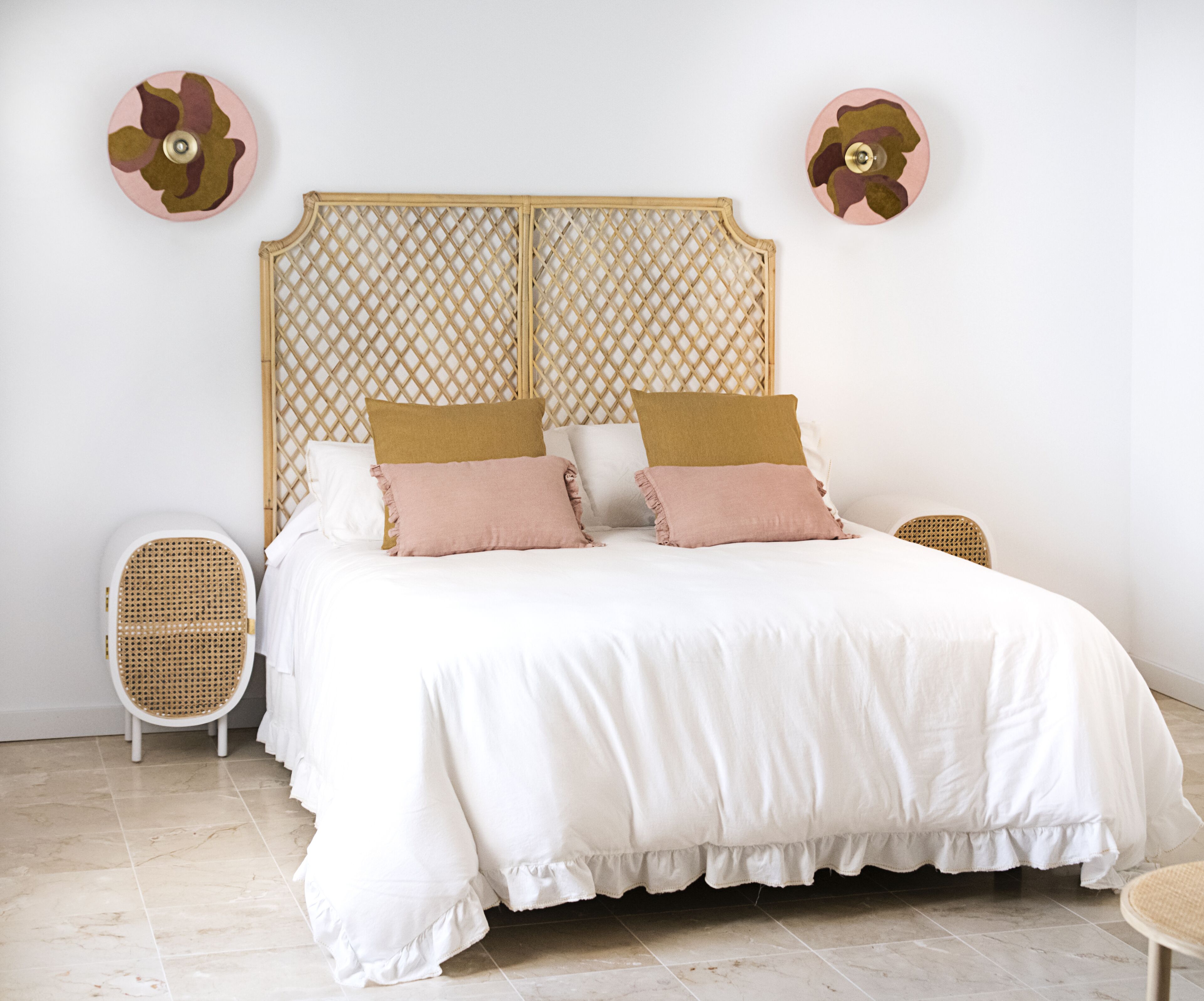Uma cama com cabeceira de madeira, duas cadeiras de vime e decoração na parede.