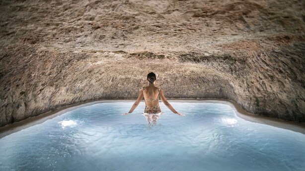 Una persona en una piscina con techo que recuerda a una cueva.