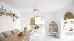 Una habitación amplia con una mesa de madera, sillas de mimbre, una hamaca colgante y vistas a través de un arco hacia un espacio exterior con una bañera.