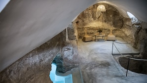 Una habitación subterránea con paredes de piedra, una lámpara colgante y una pequeña mesa con sillas.