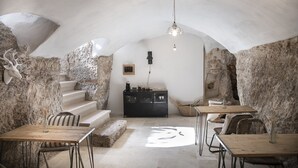 Un comedor subterráneo con paredes de piedra, mesas de madera y una escalera que conduce a un nivel superior.